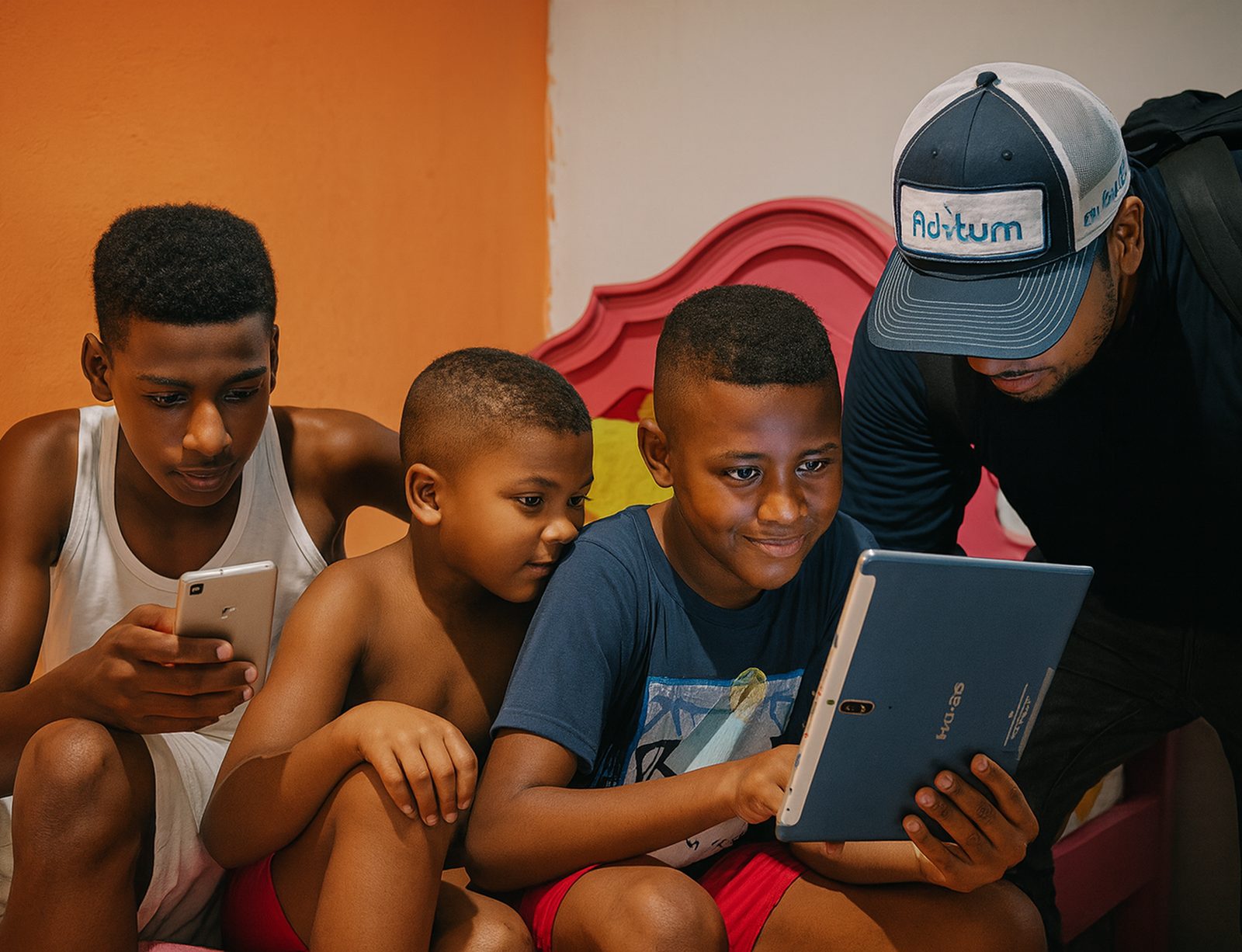 Niños conectados a internet en su hogar con un celular y una tablet, acompañados por un técnico de Aditum